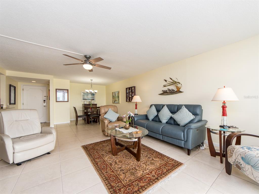 A living room with tile flooring, a blue sofa, a beige recliner, and a dining area — 675 S GULFVIEW BOULEVARD UNIT 902, CLEARWATER BEACH, FL