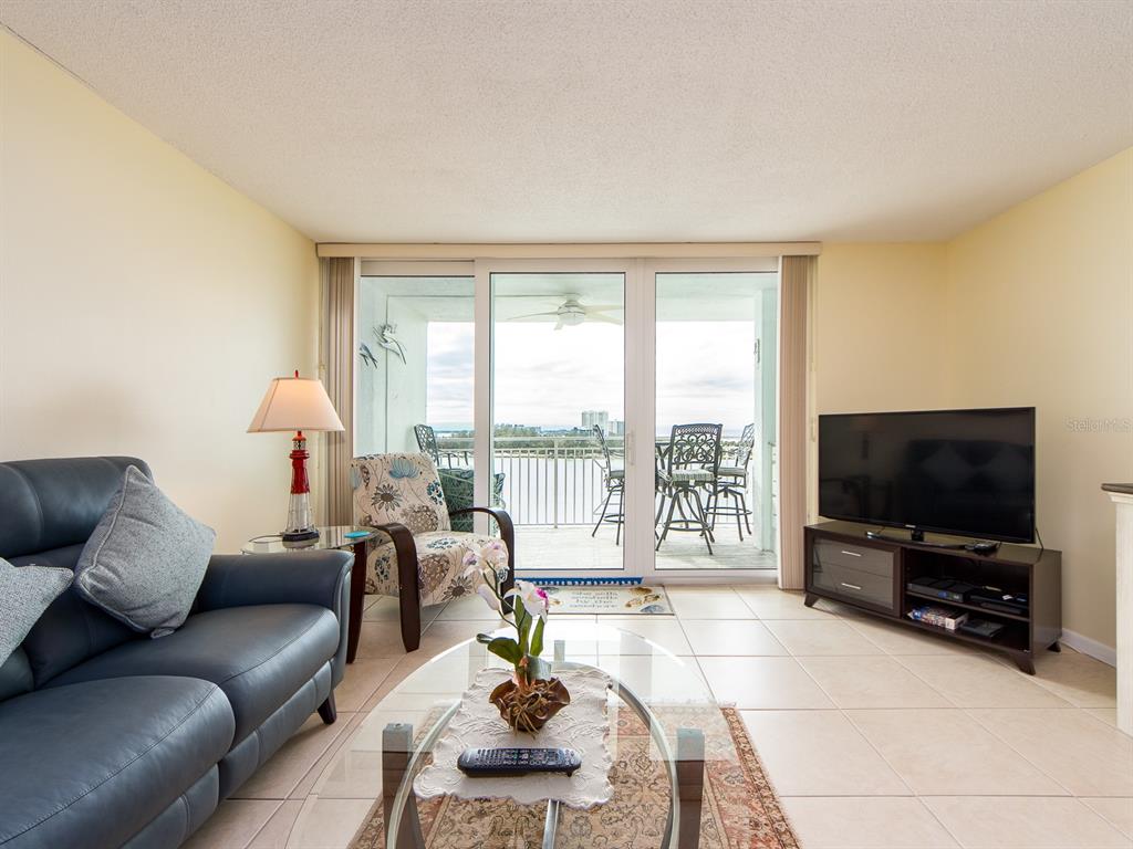 A living room with tile floors, a dark leather sofa, and a sliding glass balcony door — 675 S GULFVIEW BOULEVARD UNIT 902, CLEARWATER BEACH, FL