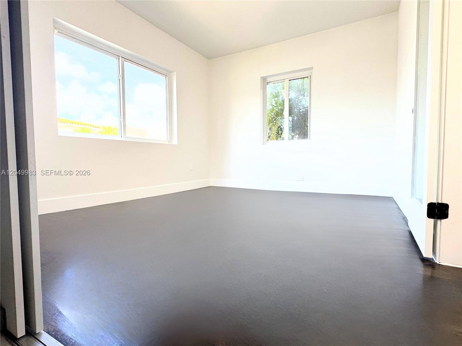 An empty room features white walls, two windows, and dark, polished flooring — 7325 Byron Ave # 8, Miami Beach FL 33141, MIAMI BEACH, FL