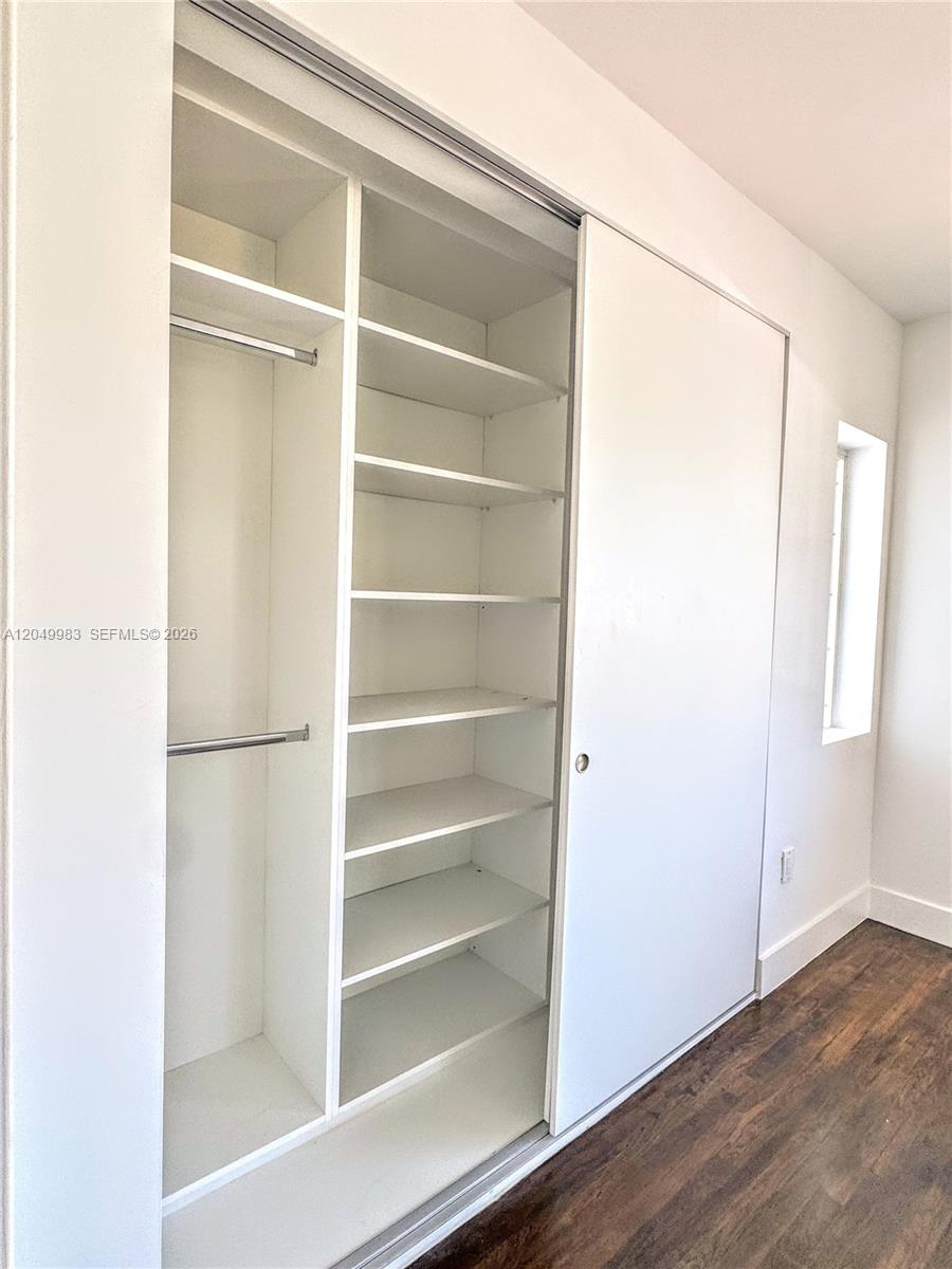 A bedroom closet features white shelving, hanging rods, and sliding doors over wood flooring — 7325 Byron Ave # 8, Miami Beach FL 33141, MIAMI BEACH, FL