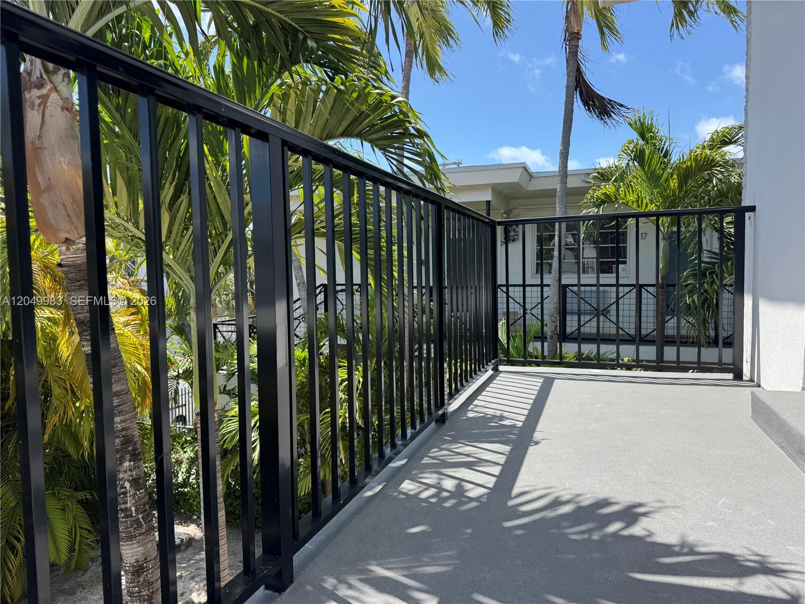 A black metal railing encloses a concrete balcony surrounded by palm trees — 7325 Byron Ave # 8, Miami Beach FL 33141, MIAMI BEACH, FL