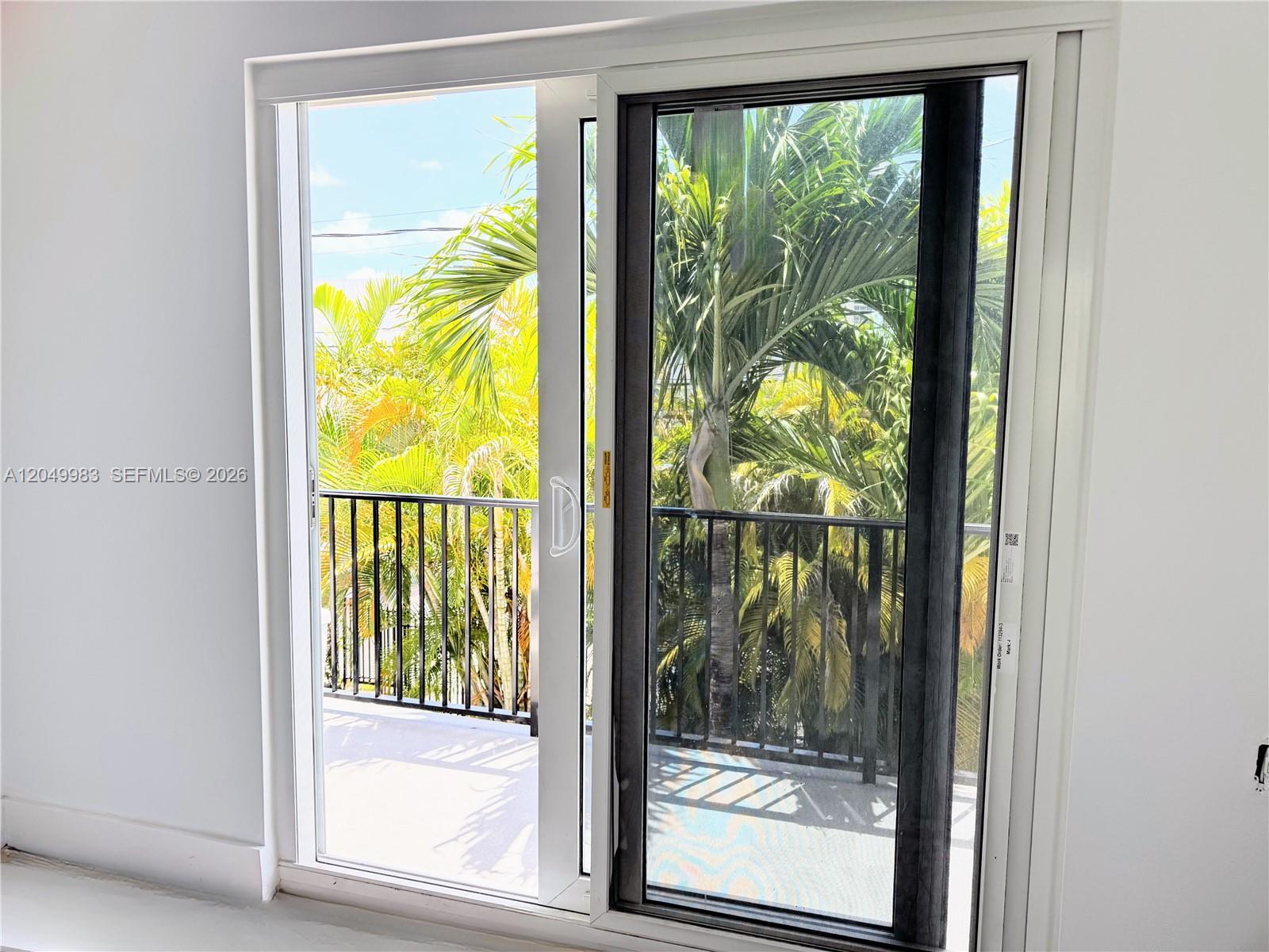 A sliding glass door opens to a balcony with a black railing and palm trees — 7325 Byron Ave # 8, Miami Beach FL 33141, MIAMI BEACH, FL