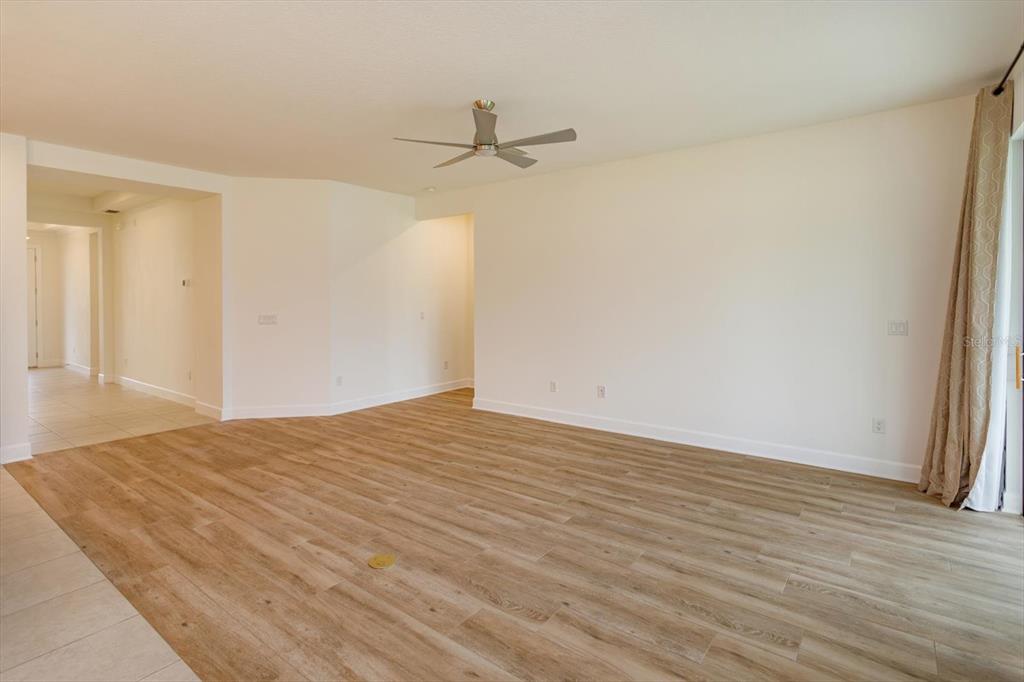 An empty living room features light wood-look flooring, a ceiling fan, and white walls — 1355 ZEEK RIDGE STREET, CLERMONT, FL