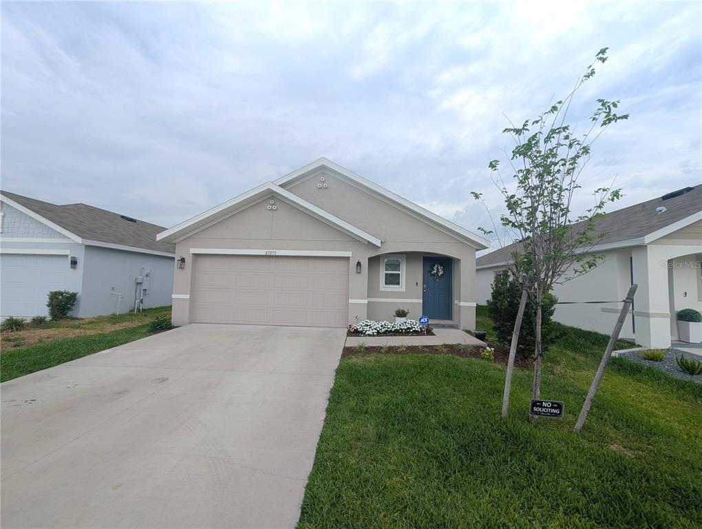 A single-story suburban house with a beige stucco exterior, a two-car garage, and a driveway — 37377 ANGEL WINGS AVENUE, ZEPHYRHILLS, FL