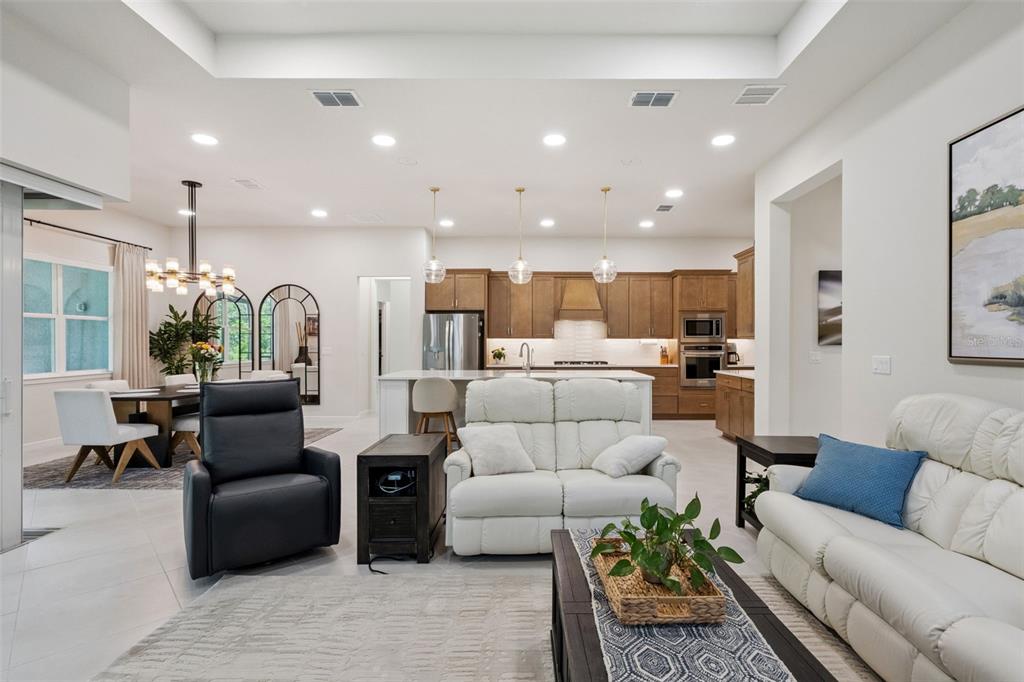 An open-concept living room and kitchen featuring white leather furniture, wood cabinetry, and tile flooring — 6524 SHIMMERING SHORES LANE, ST CLOUD, FL