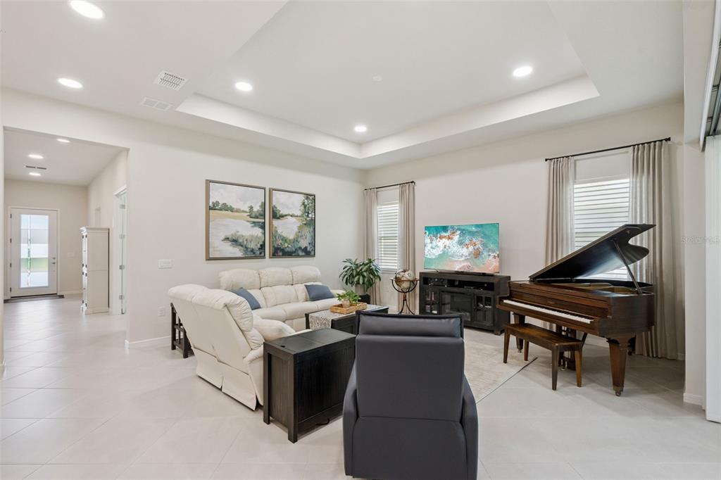 A living room features a white sofa, a dark recliner, and a grand piano — 6524 SHIMMERING SHORES LANE, ST CLOUD, FL