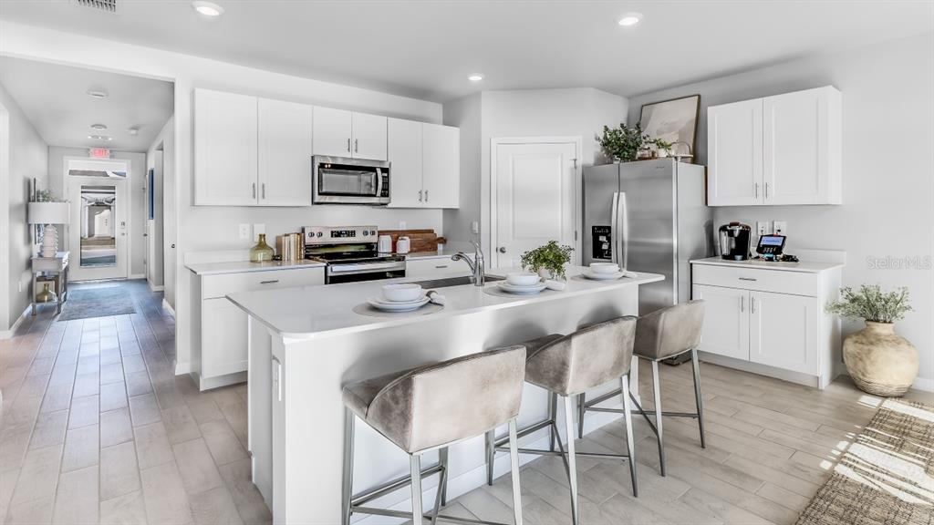 A modern kitchen features white cabinets, stainless steel appliances, a central island, and bar seating — 25252 ALCAZAR DRIVE, PUNTA GORDA, FL