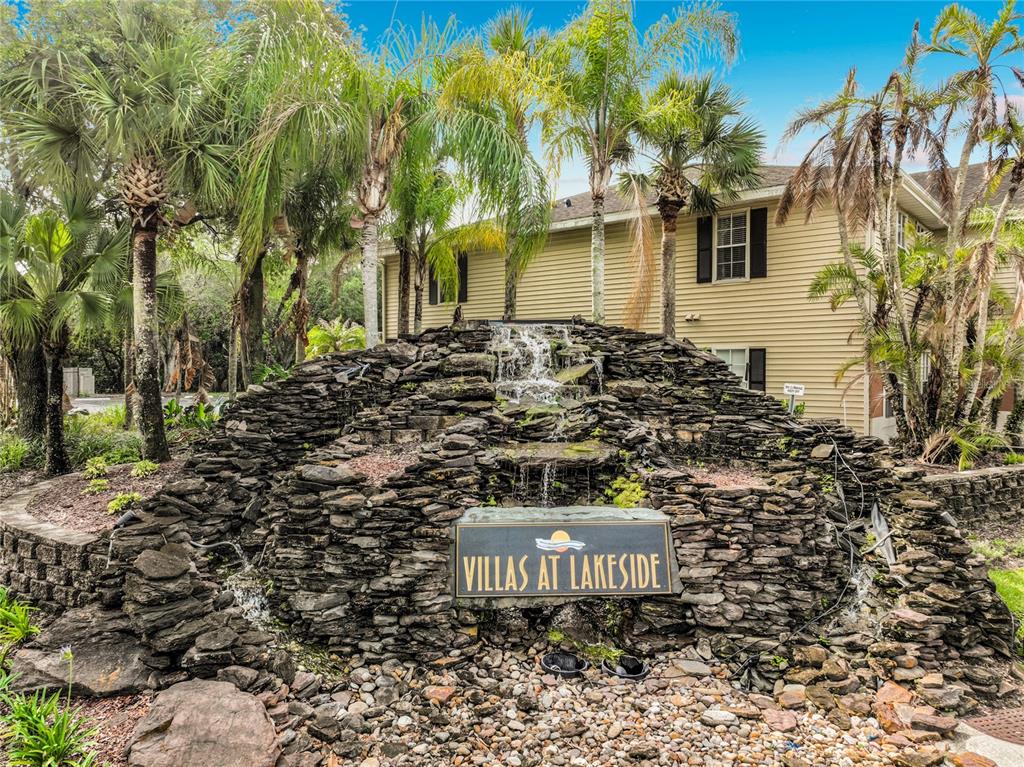 A stone waterfall feature sits in front of a two-story beige apartment building — 1909 SUMMER CLUB DRIVE UNIT 301, OVIEDO, FL