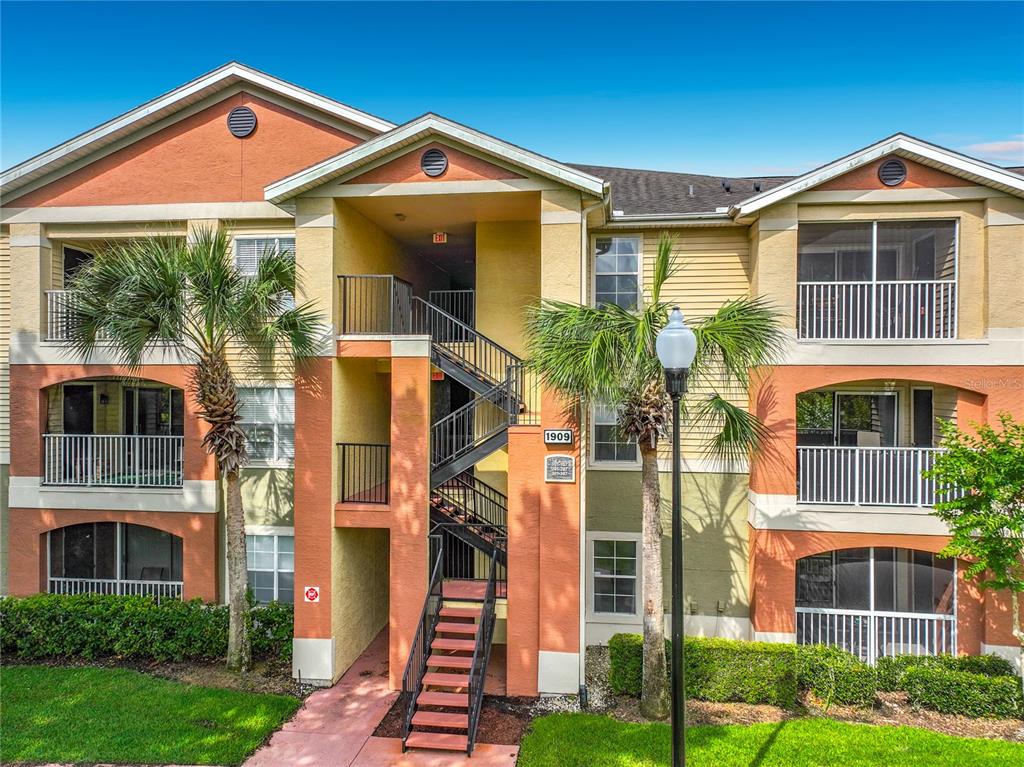 A three-story apartment building exterior features a central staircase, balconies, and palm trees — 1909 SUMMER CLUB DRIVE UNIT 301, OVIEDO, FL