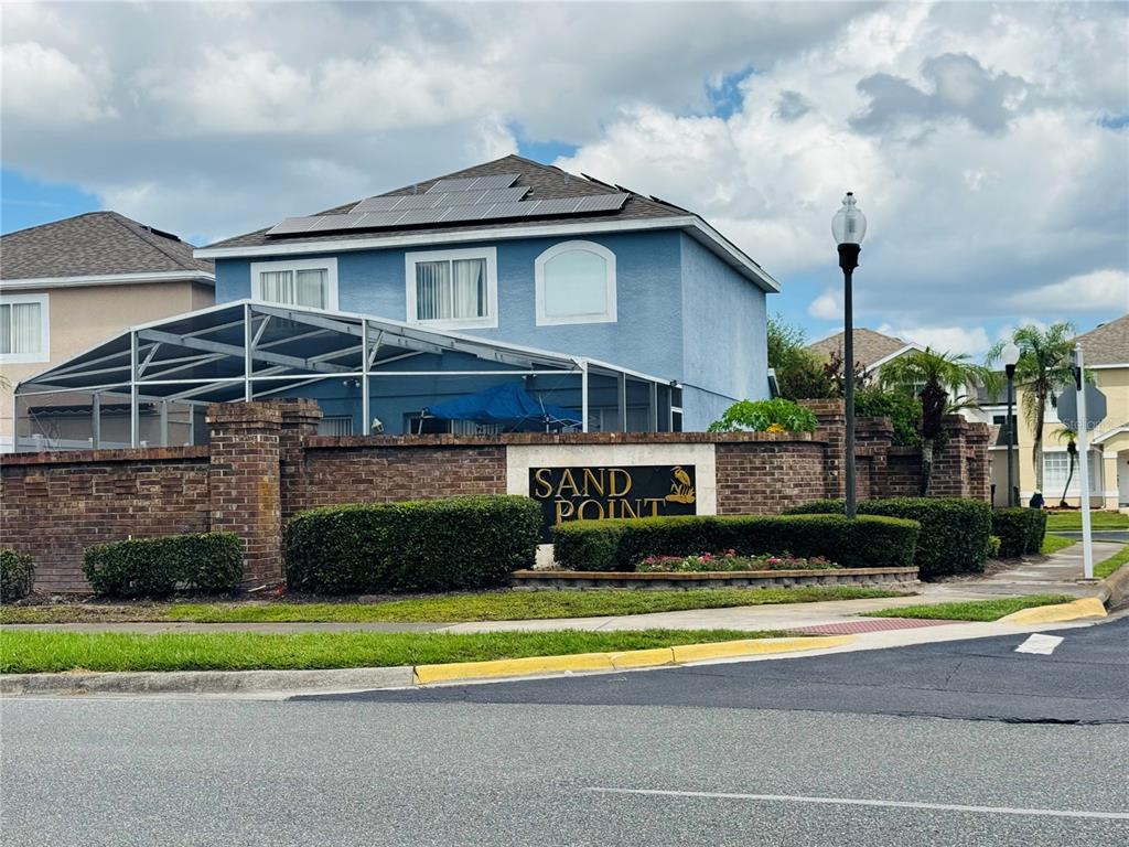 A blue two-story house with solar panels sits behind a brick wall and landscaping — 1203 SANDESTIN WAY, ORLANDO, FL
