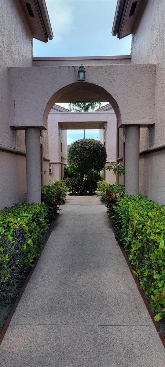A concrete walkway leads through a stucco archway between two buildings toward a landscaped courtyard — 5299 Europa Drive # P, Boynton Beach FL 33437, BOYNTON BEACH, FL