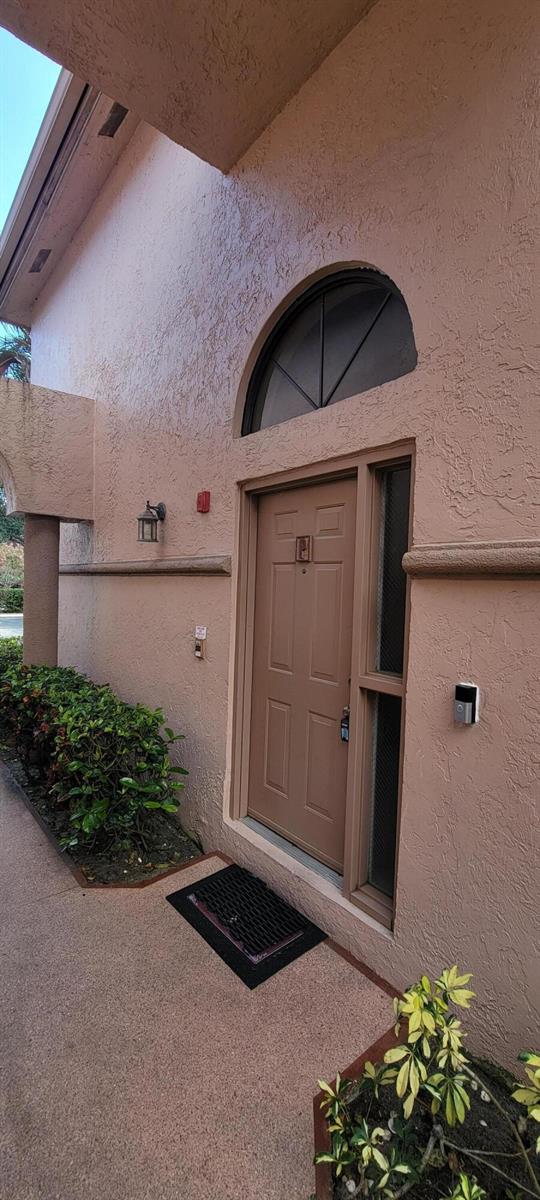 A tan stucco building exterior features a brown front door with a sidelight and arch — 5299 Europa Drive # P, Boynton Beach FL 33437, BOYNTON BEACH, FL