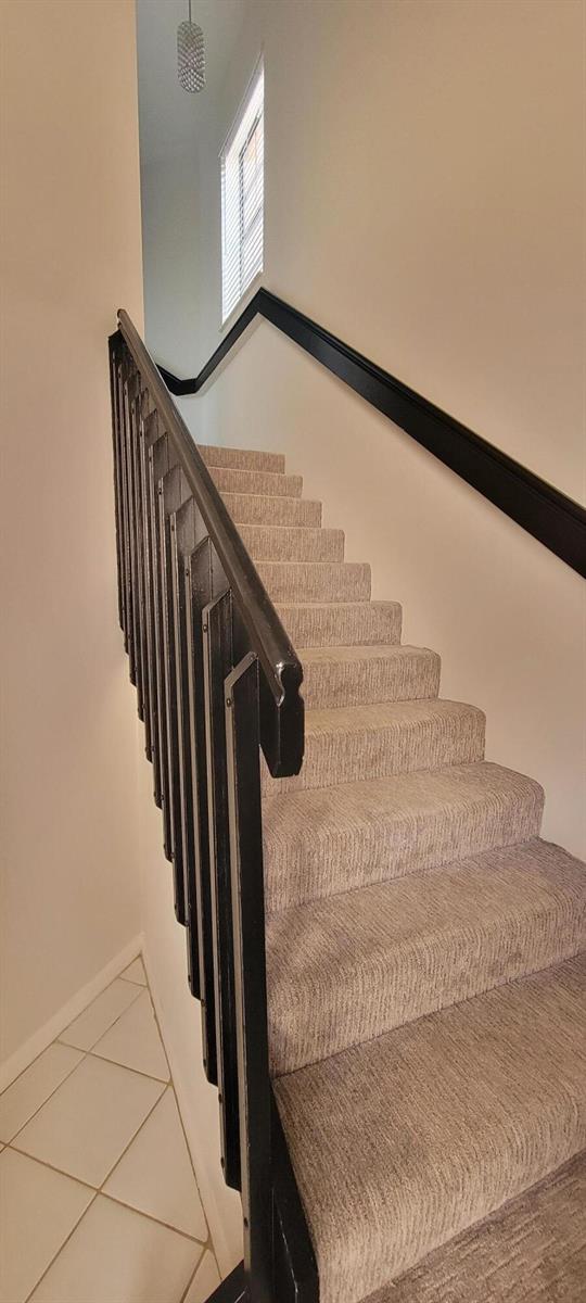 A staircase with carpeted steps and a black wooden railing leads to an upper landing — 5299 Europa Drive # P, Boynton Beach FL 33437, BOYNTON BEACH, FL