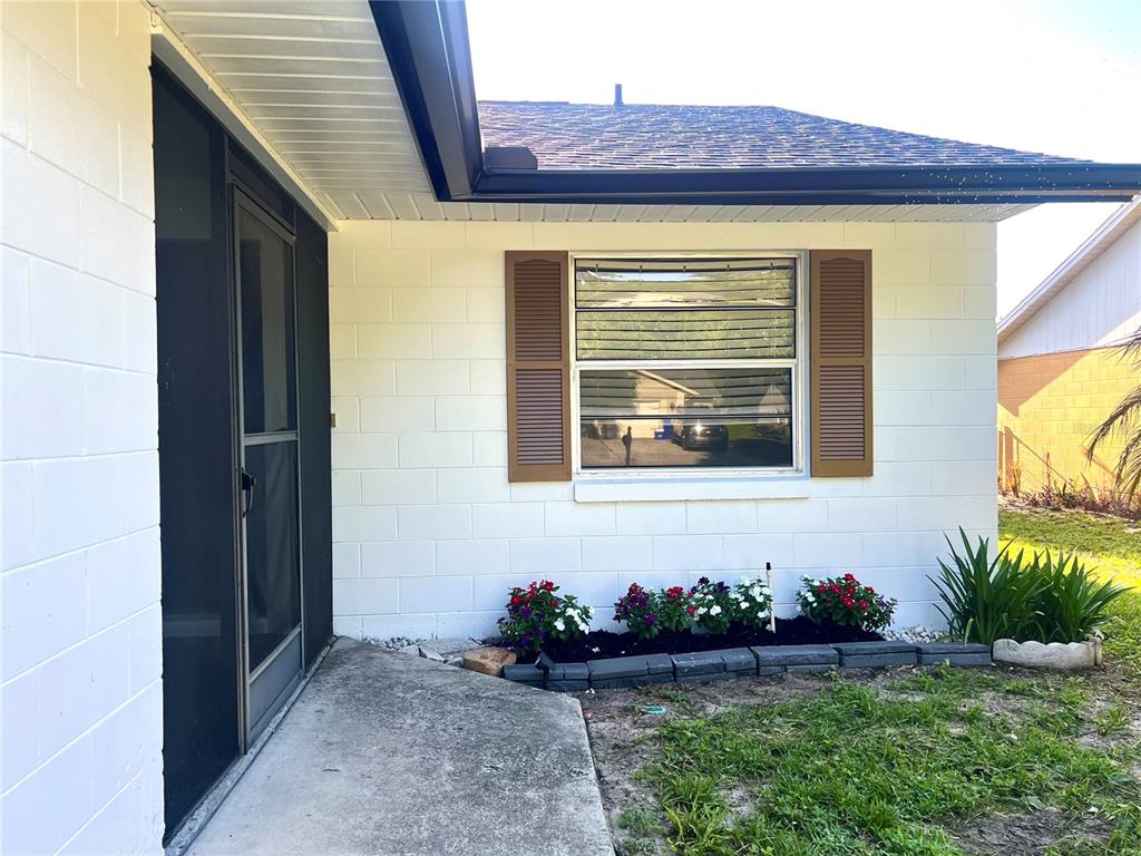 A white concrete block house exterior features a screen door, window with shutters, and landscaping — 816 SLEEPY HARBOUR DRIVE, OCOEE, FL