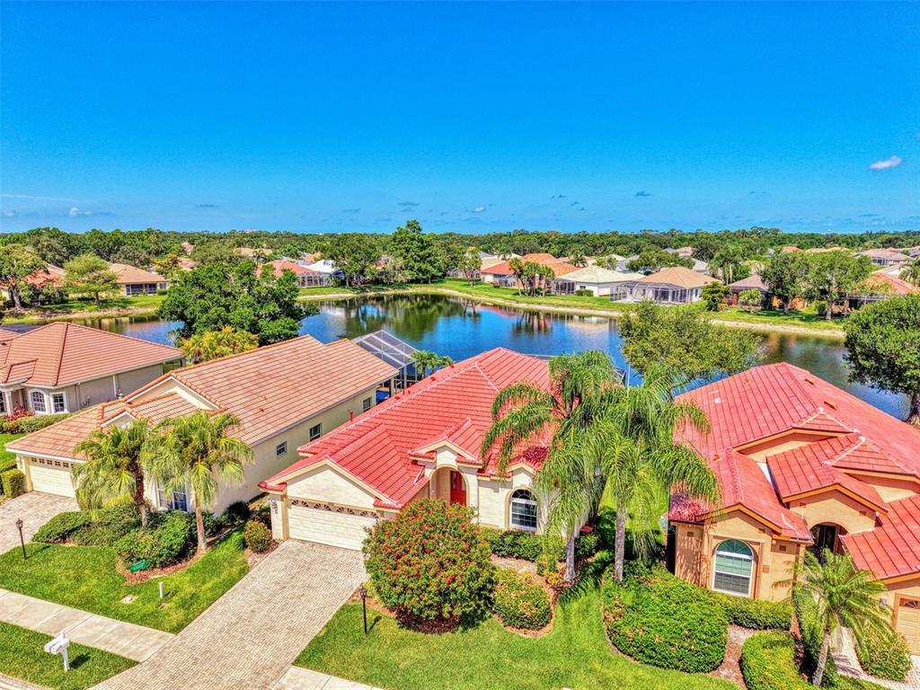 An aerial view of a suburban neighborhood featuring houses with red tile roofs near a lake — 5153 HIGHBURY CIRCLE, SARASOTA, FL