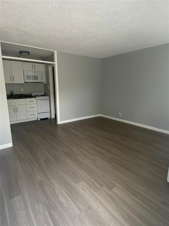 A kitchen with white cabinets and appliances opens into a living area with wood flooring — 515 BON AIR STREET UNIT 155, LAKELAND, FL