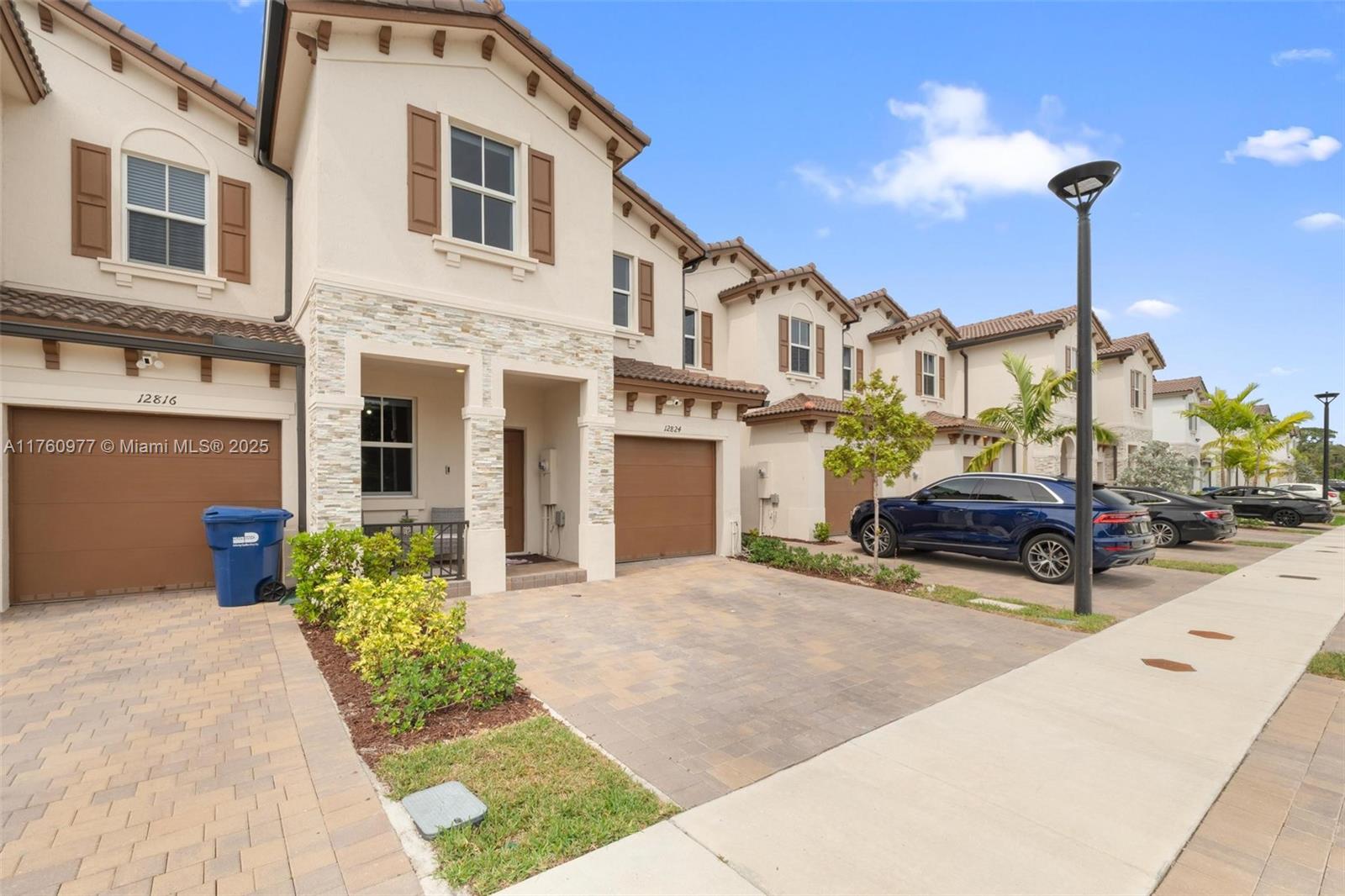 A row of two-story townhouses features beige stucco facades, brown garage doors, and paved driveways — 12824 NW 22nd Pl # 12824, Miami FL 33167, MIAMI, FL