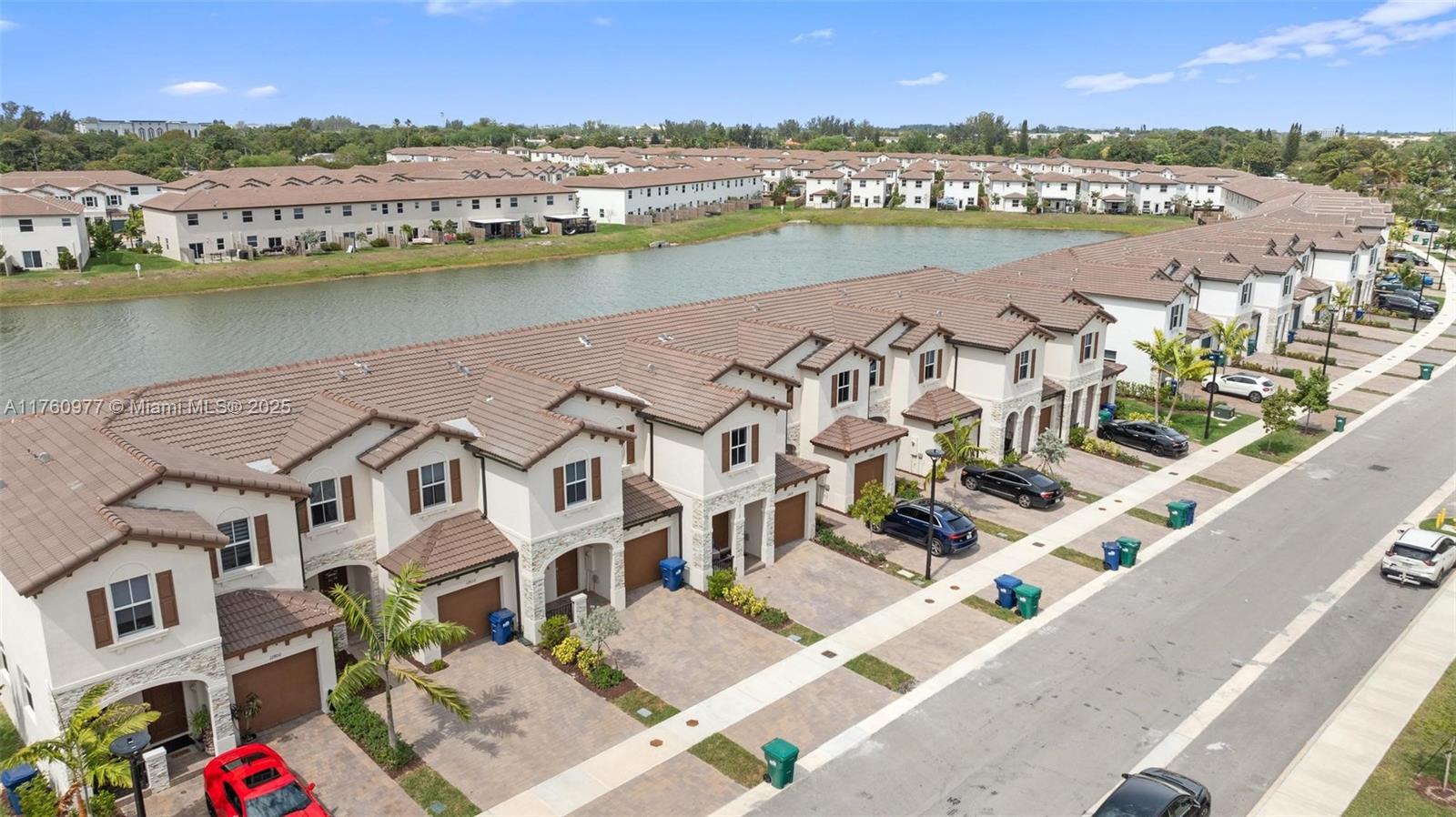 An aerial view shows a row of multi-story townhouses with tile roofs bordering a lake — 12824 NW 22nd Pl # 12824, Miami FL 33167, MIAMI, FL