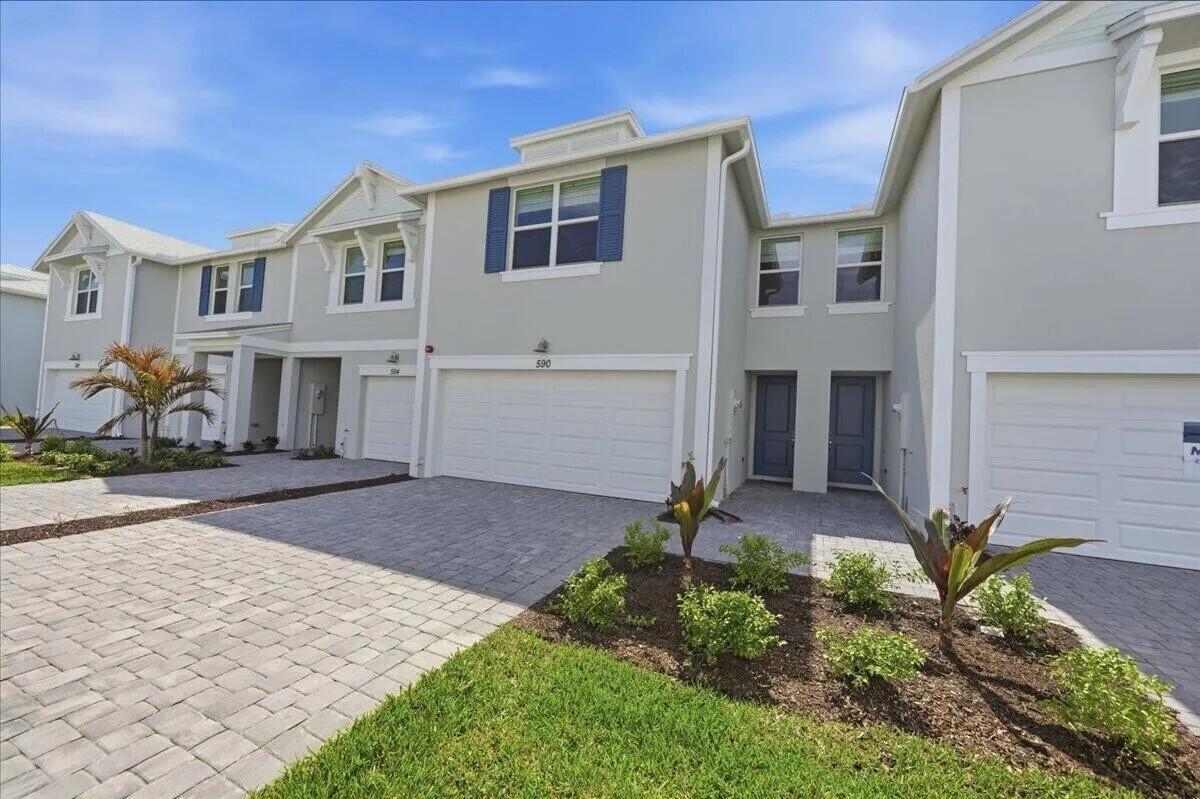 A light-colored townhome exterior features a two-car garage, paved driveway, and small landscaped garden — 590 Salisbury Circle, Fort Pierce FL 34982, FORT PIERCE, FL