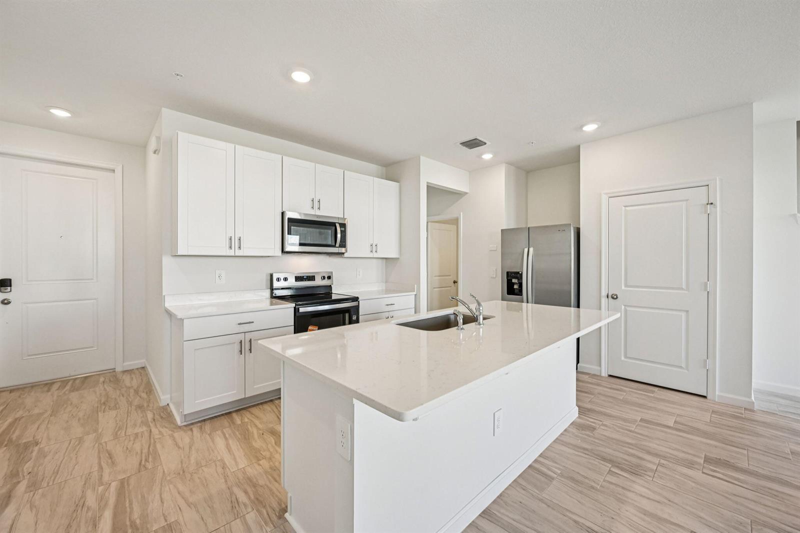A modern kitchen features white cabinets, stainless steel appliances, a quartz island, and wood-look flooring — 590 Salisbury Circle, Fort Pierce FL 34982, FORT PIERCE, FL