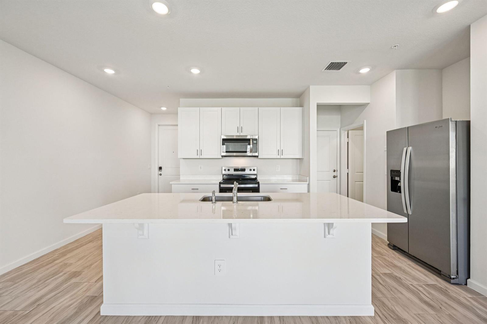 A modern kitchen features a white island, stainless steel appliances, and light wood-look flooring — 590 Salisbury Circle, Fort Pierce FL 34982, FORT PIERCE, FL