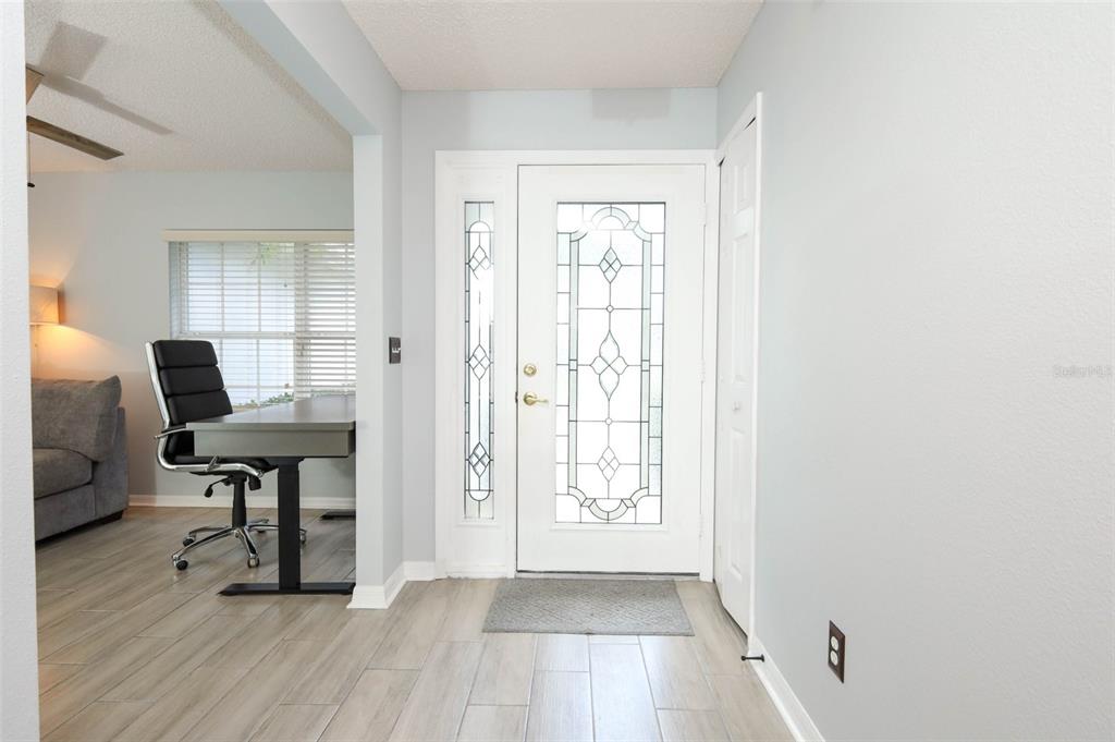 An entryway features a white front door with decorative glass, light wood-look tile, and walls — 3598 ROLLINGBROOK STREET, CLERMONT, FL