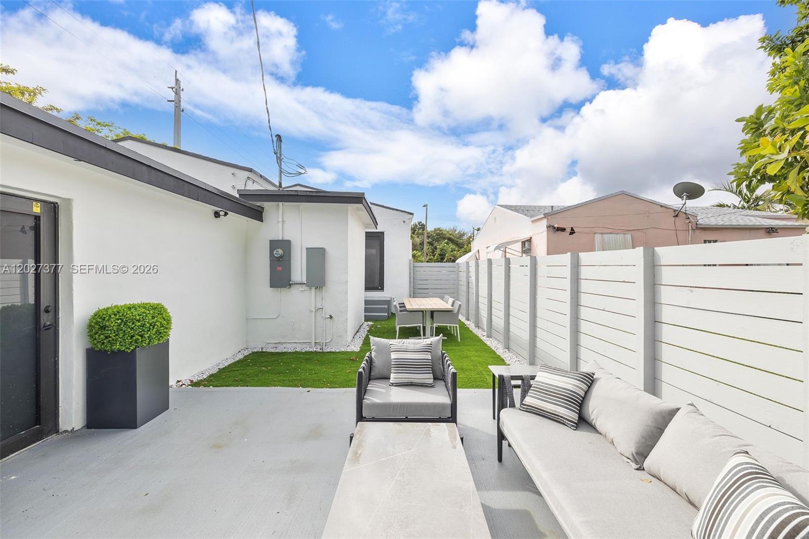 A fenced backyard features a patio with outdoor furniture, artificial turf, and a dining area — 501 NW 46th St, Miami FL 33127, MIAMI, FL