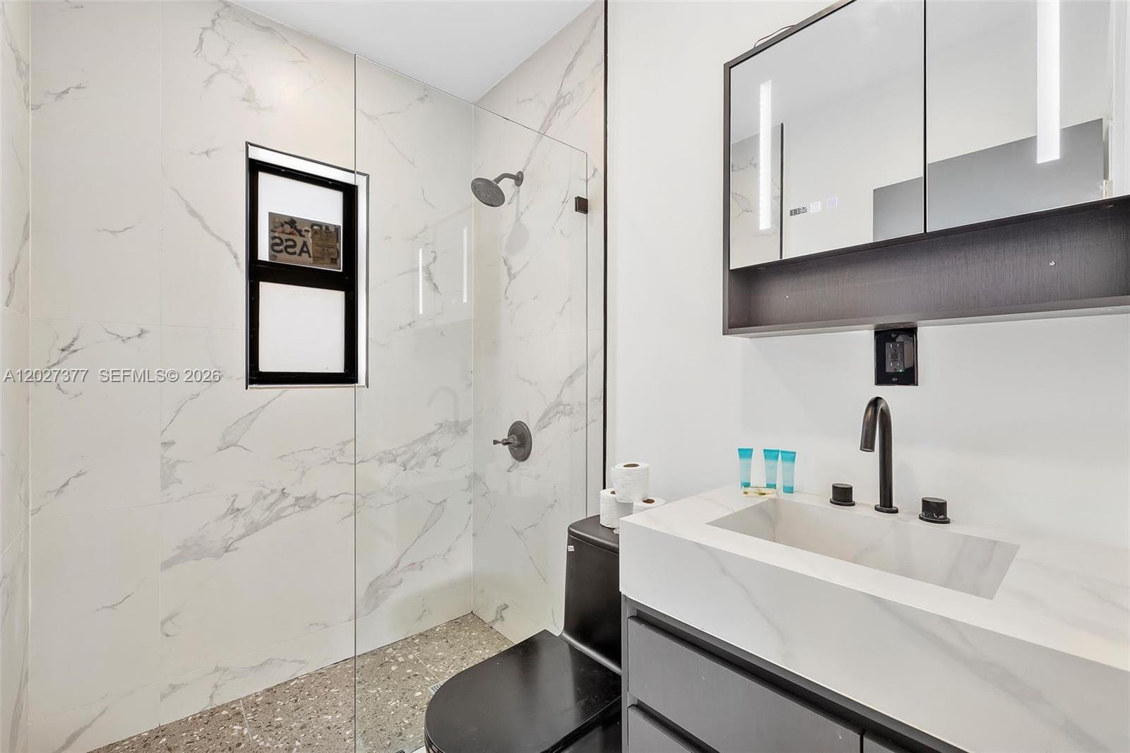 A modern bathroom features a marble-tiled walk-in shower, a black toilet, and a vanity — 501 NW 46th St, Miami FL 33127, MIAMI, FL
