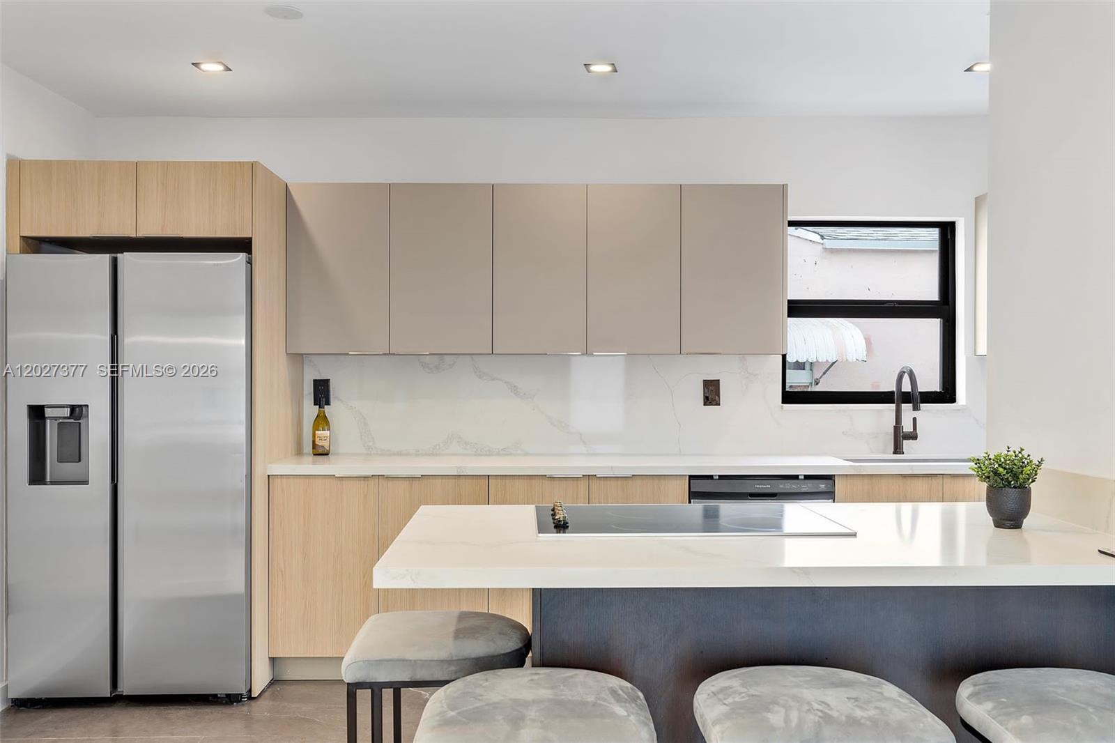 A modern kitchen features light wood cabinets, gray upper cabinets, a white island, and stainless appliances — 501 NW 46th St, Miami FL 33127, MIAMI, FL