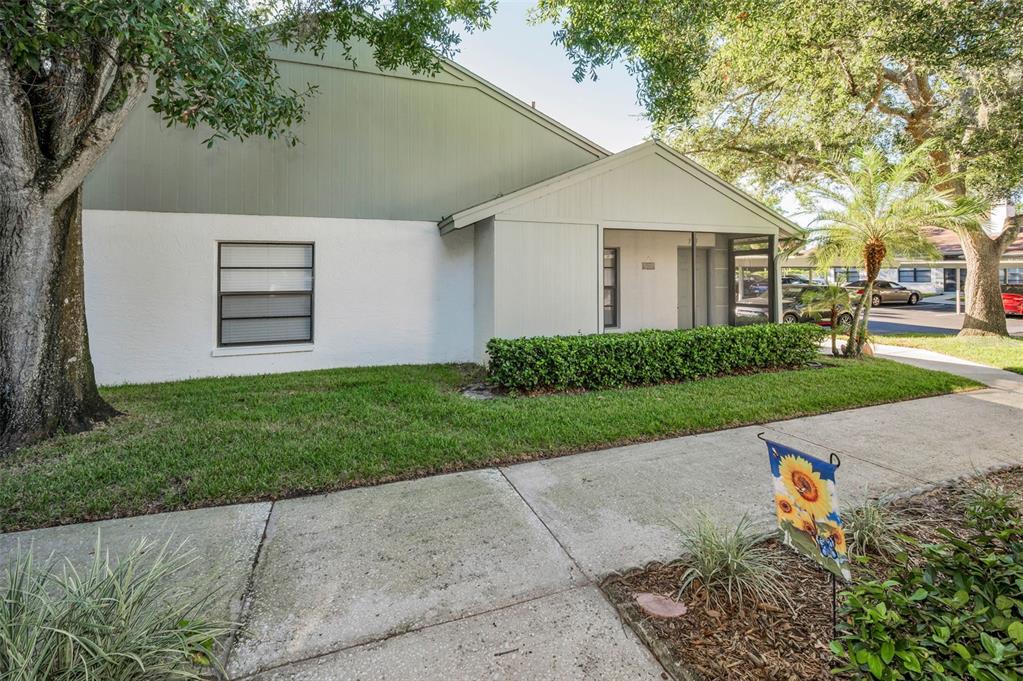 A single-story residential building with white stucco walls, a green gable, and a screened entryway — 3500 MAGNOLIA RIDGE CIRCLE UNIT 405, PALM HARBOR, FL