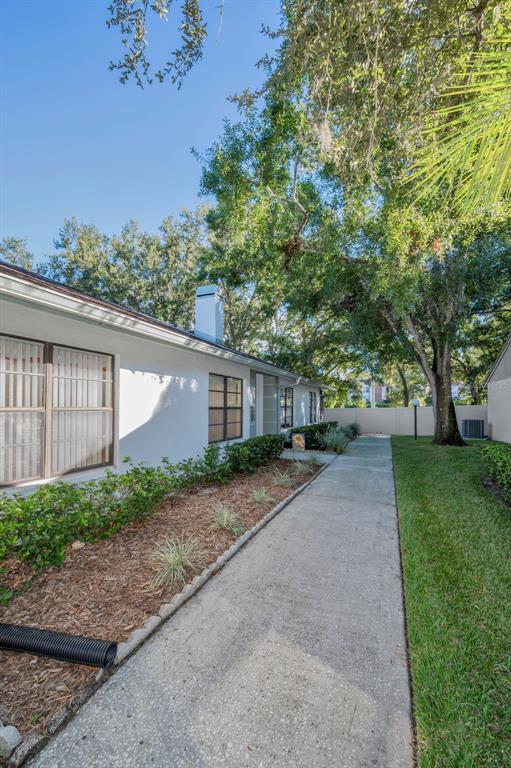 A concrete walkway runs alongside a white building with a chimney and landscaped garden beds — 3500 MAGNOLIA RIDGE CIRCLE UNIT 405, PALM HARBOR, FL