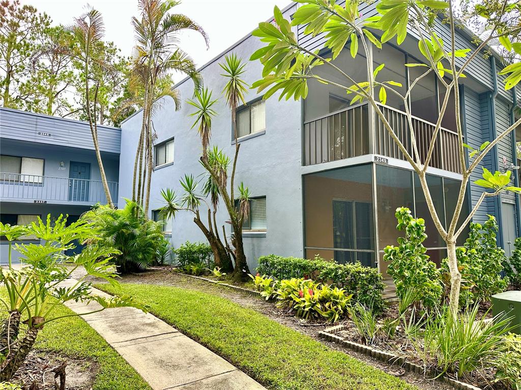 A two-story blue apartment building with screened balconies and tropical landscaping along a walkway — 2349 OAK PARK WAY UNIT 107, ORLANDO, FL