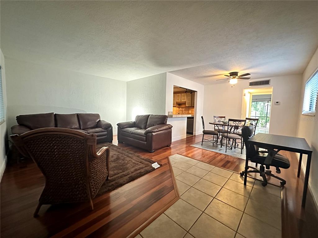 An open-concept living and dining area features wood flooring, tiled entryway, and dark leather furniture — 2349 OAK PARK WAY UNIT 107, ORLANDO, FL