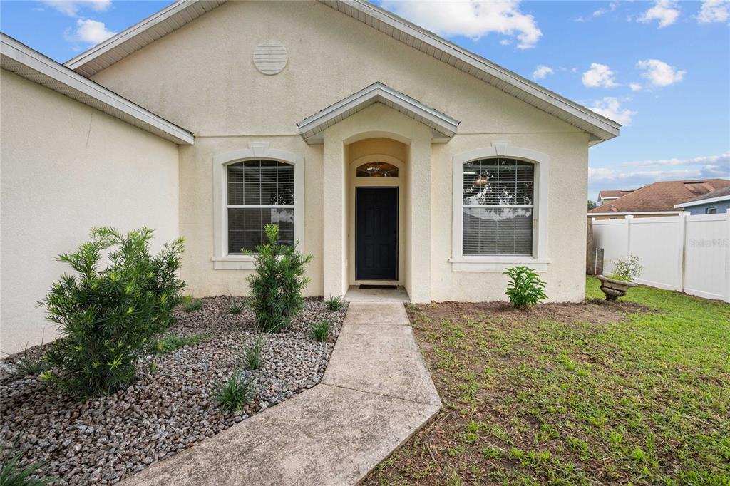 The exterior of a beige stucco house features a concrete walkway leading to the front door — 2556 SE 75TH BOULEVARD, BUSHNELL, FL