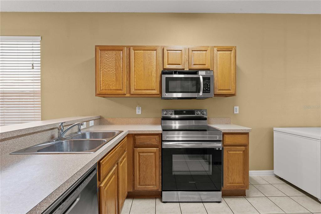 A kitchen features oak cabinets, stainless steel appliances, a double sink, and tiled flooring — 2556 SE 75TH BOULEVARD, BUSHNELL, FL