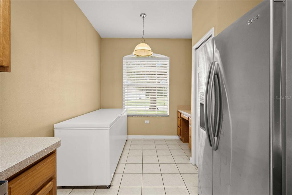 A kitchen features a chest freezer, tile flooring, a window, and a stainless steel refrigerator — 2556 SE 75TH BOULEVARD, BUSHNELL, FL
