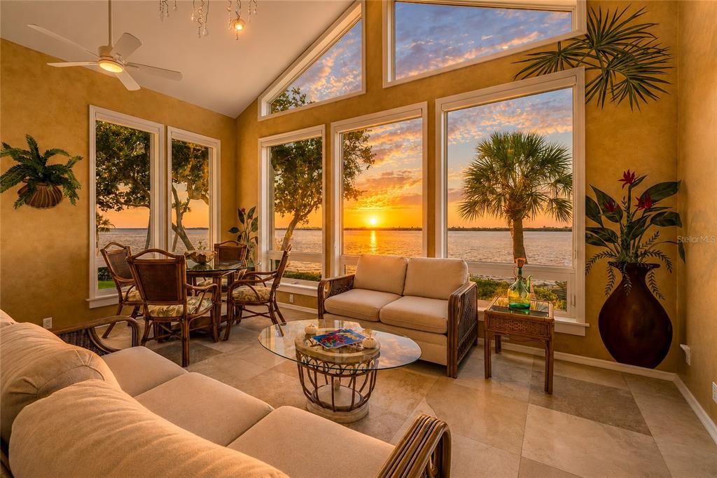 A sunroom with a beige sofa, rattan furniture, and large windows overlooking a sunset waterfront — 56 TIDY ISLAND BOULEVARD UNIT 56, BRADENTON, FL