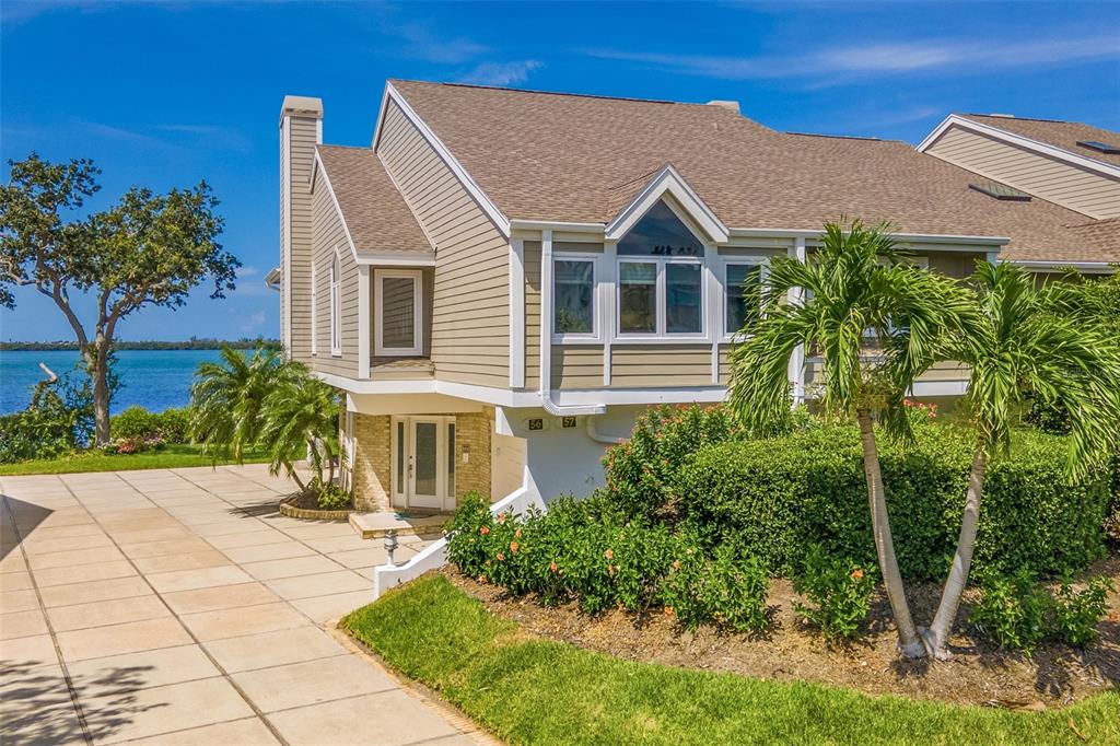 A tan, two-story waterfront townhouse features a paved driveway, palm trees, and a bay view — 56 TIDY ISLAND BOULEVARD UNIT 56, BRADENTON, FL
