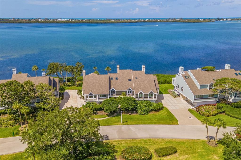 An aerial view shows waterfront townhomes with shingled roofs and driveways near a large bay — 56 TIDY ISLAND BOULEVARD UNIT 56, BRADENTON, FL