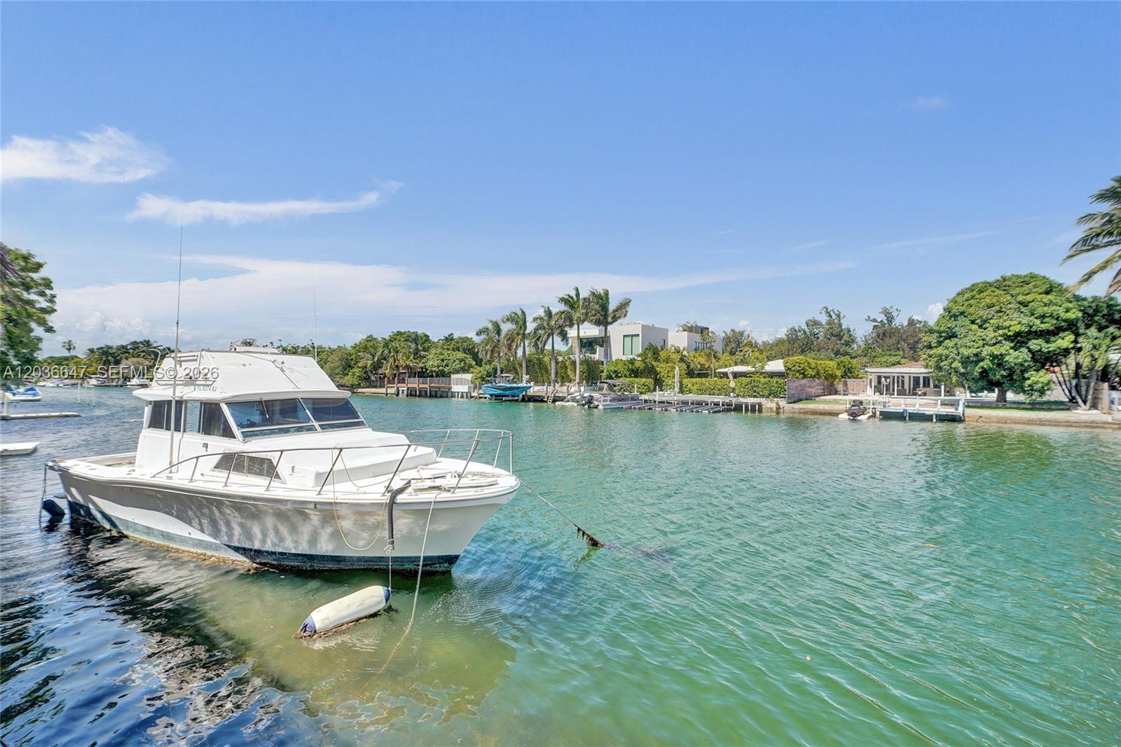 A white motorboat is moored in a canal near a shoreline with trees and houses — 1945 Calais Dr # 3, Miami Beach FL 33141, MIAMI BEACH, FL