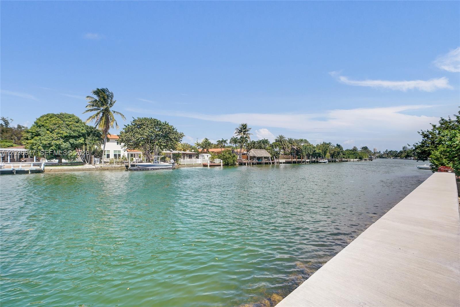 A concrete seawall borders a canal lined with houses, palm trees, and private boat docks — 1945 Calais Dr # 3, Miami Beach FL 33141, MIAMI BEACH, FL