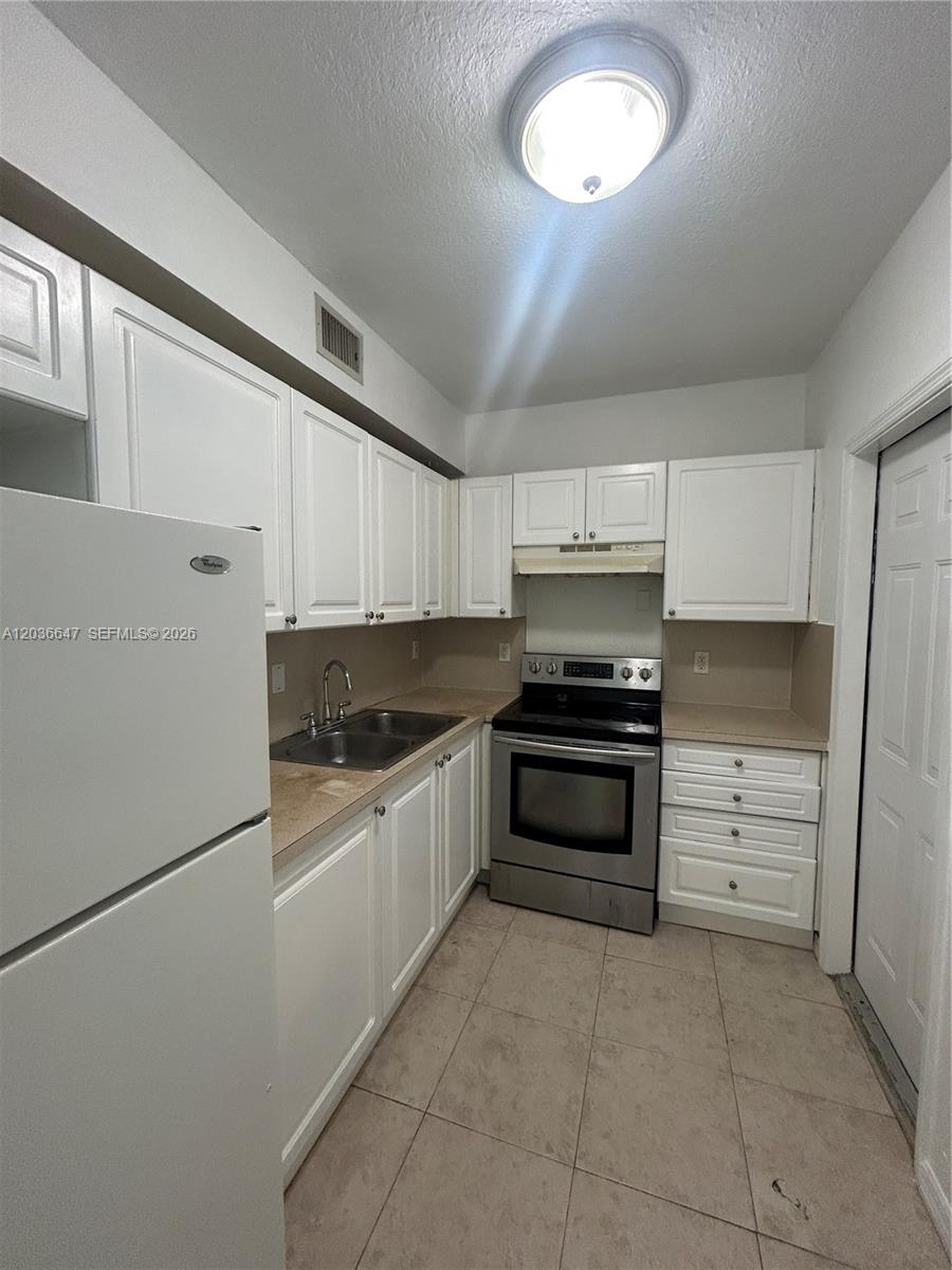 A kitchen features white cabinets, stainless steel appliances, and light-colored tile flooring — 1945 Calais Dr # 3, Miami Beach FL 33141, MIAMI BEACH, FL