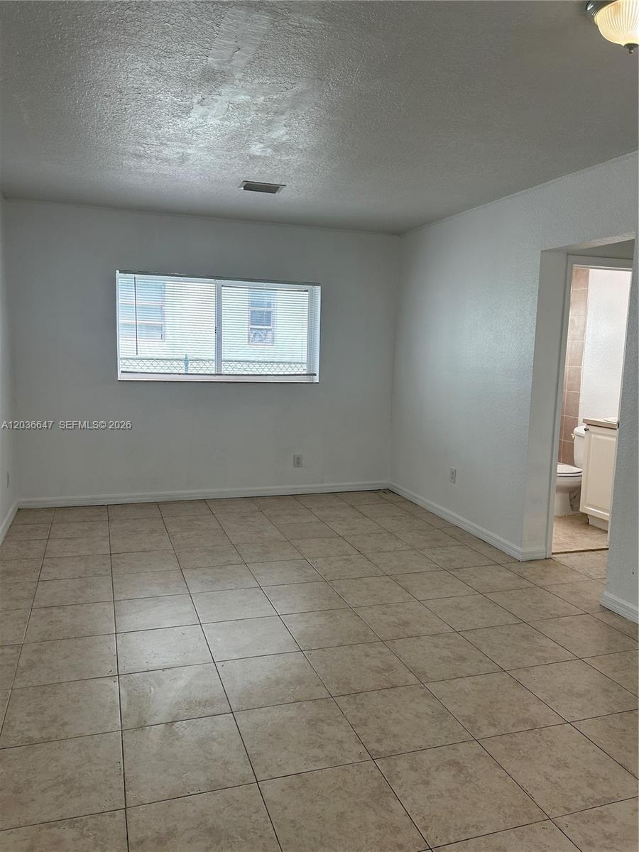 A bedroom with beige tile flooring, white walls, and an attached bathroom — 1945 Calais Dr # 3, Miami Beach FL 33141, MIAMI BEACH, FL