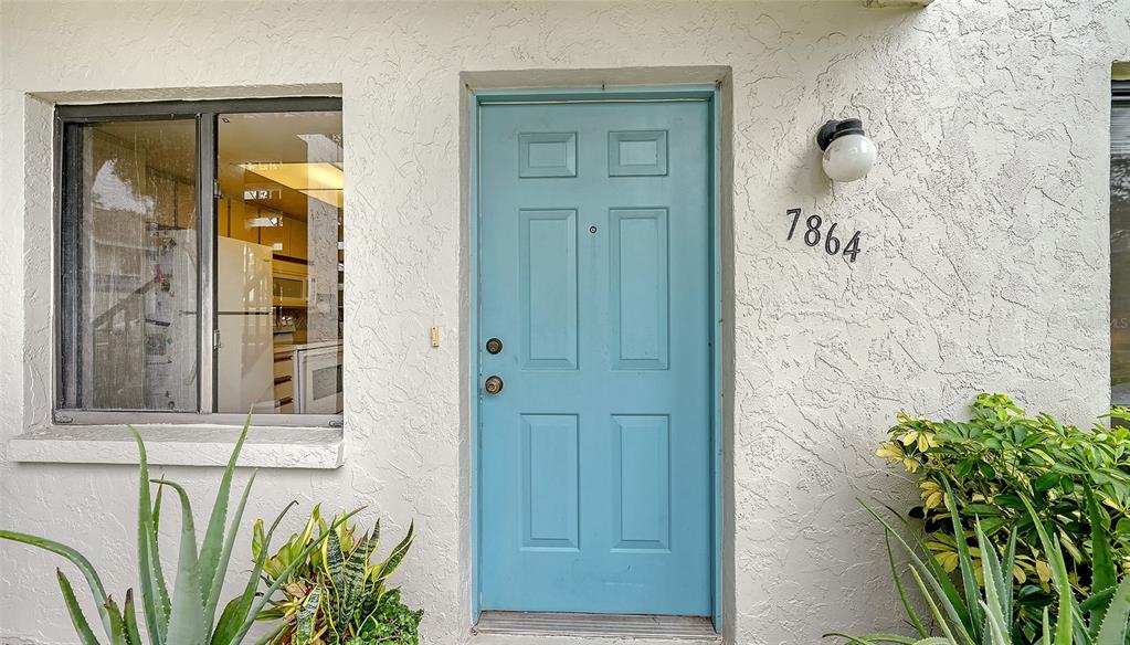 A light blue front door with a house number sits next to a window and plants — 7864 EAGLE CREEK DRIVE UNIT 7864, SARASOTA, FL