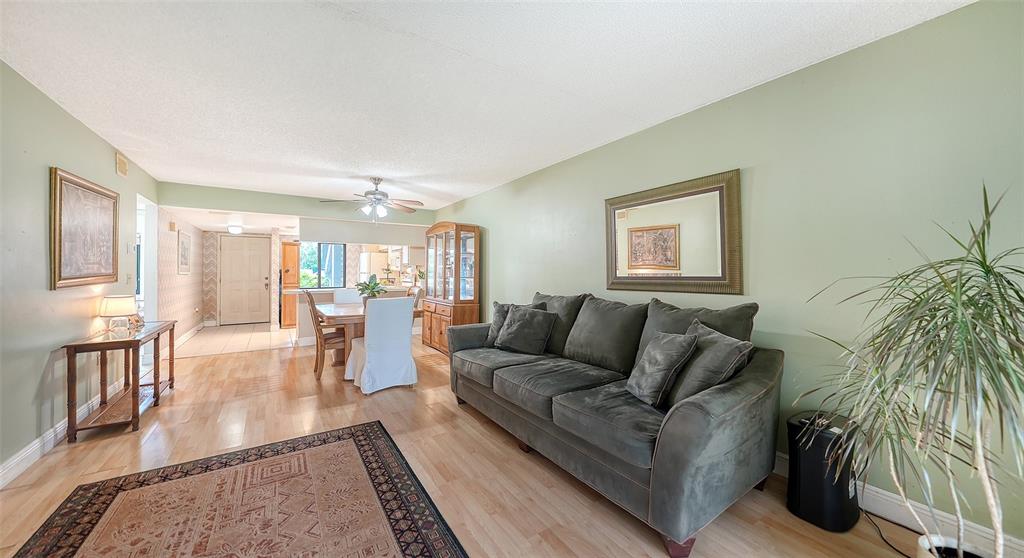 A living room with light wood floors, a green sofa, and an adjacent dining area — 7864 EAGLE CREEK DRIVE UNIT 7864, SARASOTA, FL