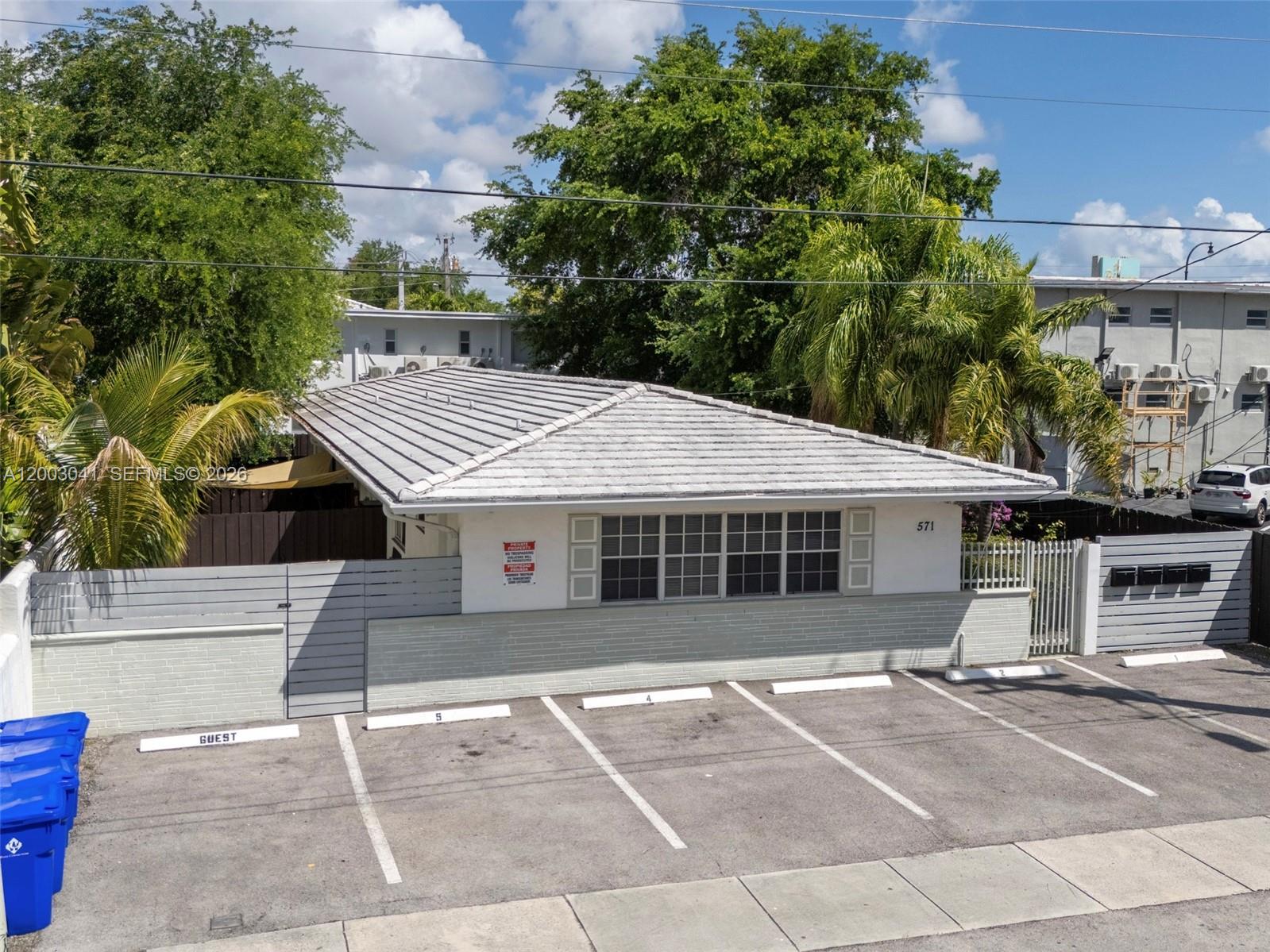An exterior view of a single-story building with a tiled roof and assigned parking spaces — 571 NE 67th St, Miami FL 33138, MIAMI, FL
