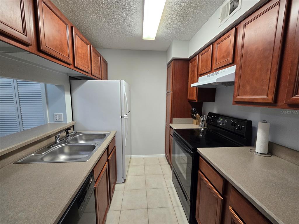 A galley kitchen features wood cabinets, laminate countertops, a white refrigerator, and black appliances — 1401 S PALMETTO AVENUE UNIT 809, DAYTONA BEACH, FL