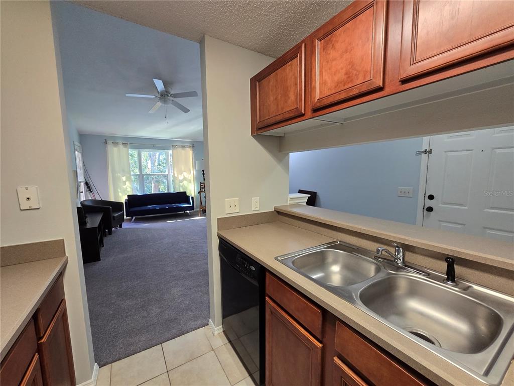 A kitchen sink and dishwasher overlook a carpeted living room with a ceiling fan — 1401 S PALMETTO AVENUE UNIT 809, DAYTONA BEACH, FL