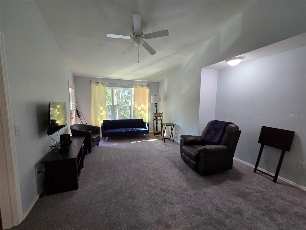 A living room features gray carpeting, a vaulted ceiling with a fan, and several seating pieces — 1401 S PALMETTO AVENUE UNIT 809, DAYTONA BEACH, FL