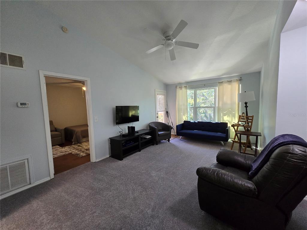 A living room features gray carpeting, a vaulted ceiling, a ceiling fan, and a television console — 1401 S PALMETTO AVENUE UNIT 809, DAYTONA BEACH, FL
